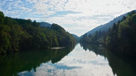 Blue-reflecting-river-mountain-in-idyllic-landscape-bathed-in-sunlight,-mountains-background,-cloudy-blue-sky