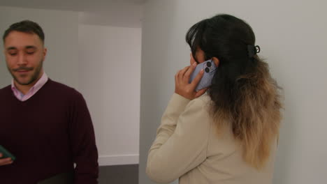 maestra hablando por teléfono móvil pasando a un colega masculino mientras caminan por el corredor en el edificio de la escuela