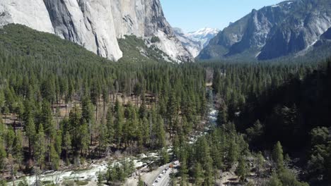 a fast moving river stream winding through the valley floor of yosemite national park. spring to summer tourist season, slow aerial tilt up towards the famous granite mountain skyline.