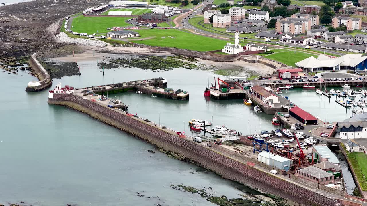 Drone footage glides over fishing harbor, marina, and dockyard under overcast daylight in Dundee