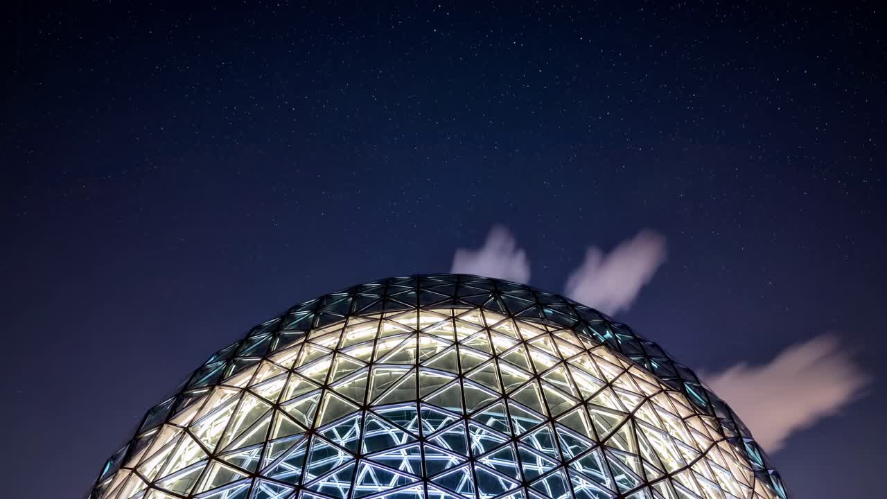 Modern glass dome structure illuminating the night with a mesmerizing glow, set against a backdrop of twinkling stars and wispy clouds, creating a captivating blend of architecture and nature