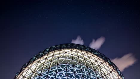 modern glass dome structure illuminating the night with a mesmerizing glow, set against a backdrop of twinkling stars and wispy clouds, creating a captivating blend of architecture and nature