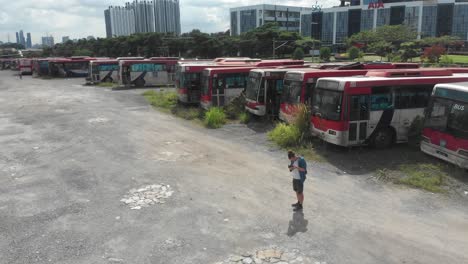 Man-standing-at-old-busses-junkyard-at-Kuala-lumpur,-aerial