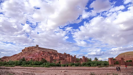 time lapse shot of aït-ben-haddou city located on hill in atlas mountains of morocco - people walking towards village - clouds flying at sky - unesco world heritage