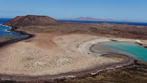 toma aerea sobre la costa y la playa de la concha en la isla de los lobos, viendo el volcan que la habita