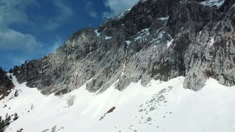 Close-flight-toward-a-glacier-rock-snow-mountain-top-near-Bavaria-Elmau-castle-in-the-Bavarian-Austrian-alps-on-a-cloudy-and-sunny-day-along-trees-and-forest-in-nature-with-avalanches-going-down