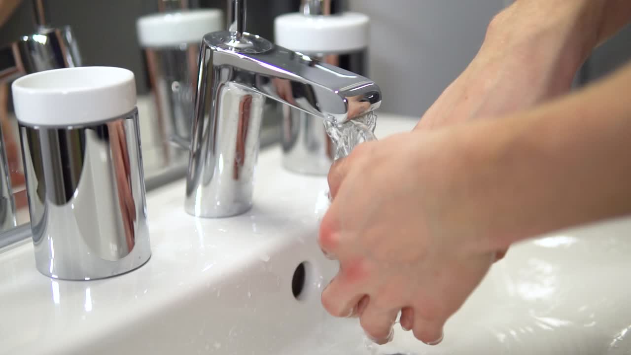 cámara lenta de hombres blancos desinfectando las manos lavándolas con agua de grifo en un baño limpio