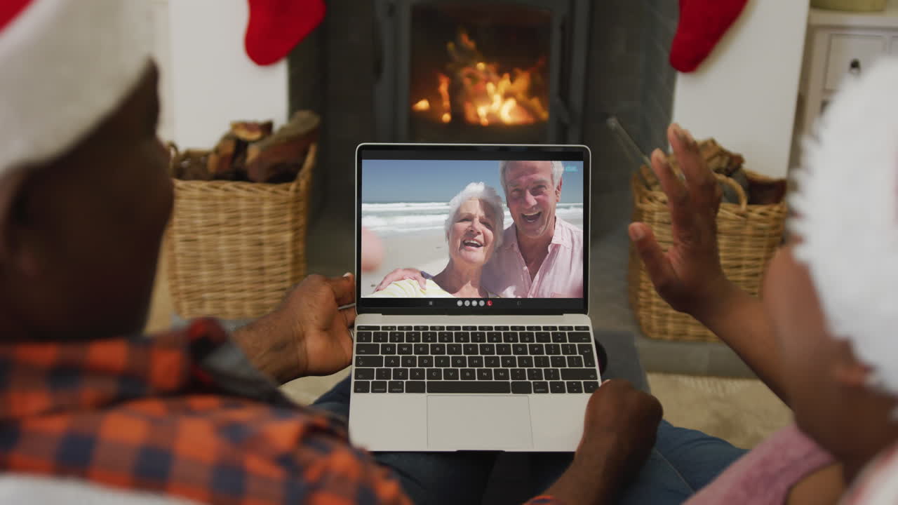 pareja afroamericana con sombreros de santa usando una computadora portátil para una videollamada de navidad con la pareja en la pantalla