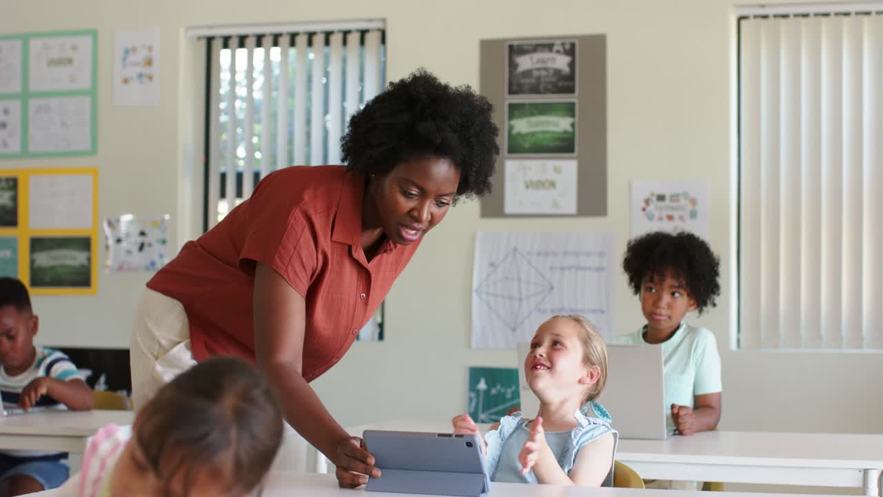 Teacher leaning over front desk in class after youth female raising hand, guiding tablet folio use