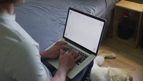 hombre caucásico usando computadora portátil en el dormitorio con perro mascota