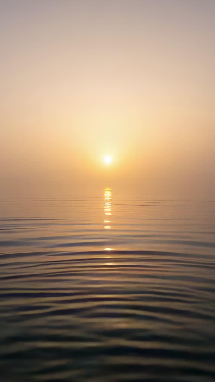 Video verticale: Sole basso splendente proietta un sentiero di luce sul mare calmo, piccole increspature si espandono dalla brezza.
