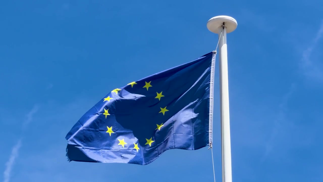 La bandiera blu dell'Unione Europea sventola con costanza da un'asta bianca sotto un sole splendente