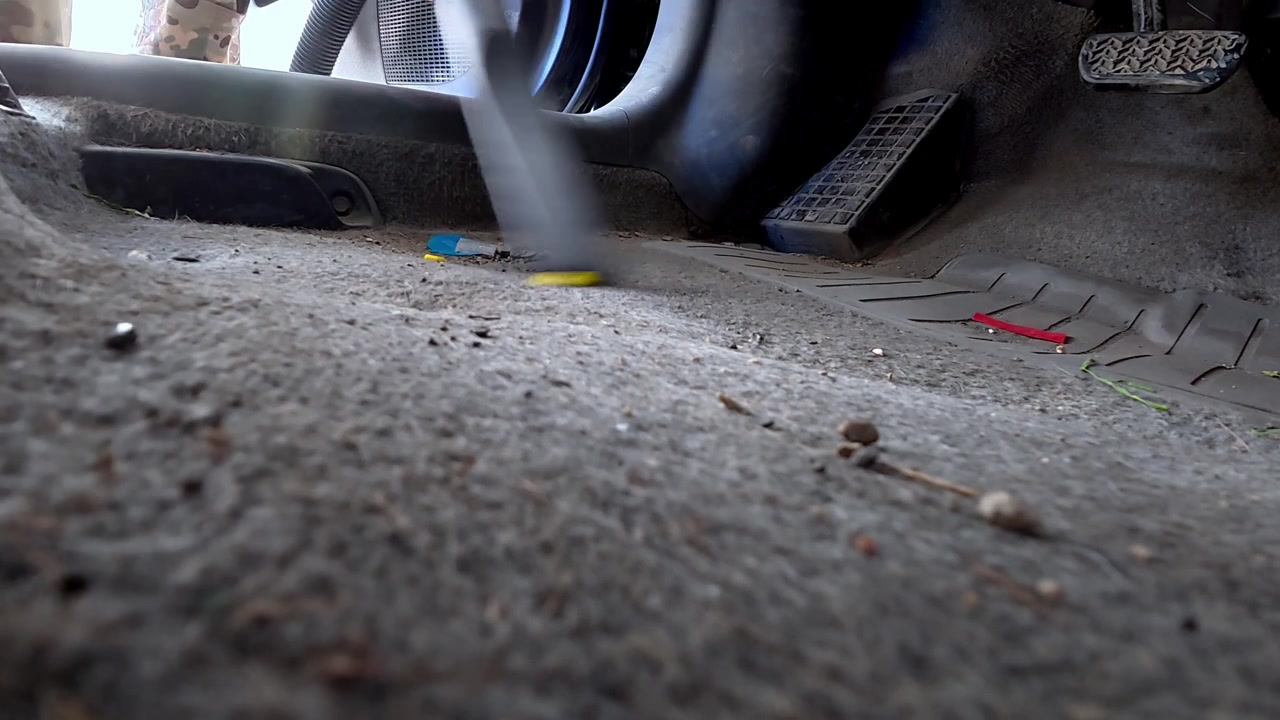 A vehicle interior is being cleaned with a portable vacuum. Dust and debris are being removed from the car’s flooring.
