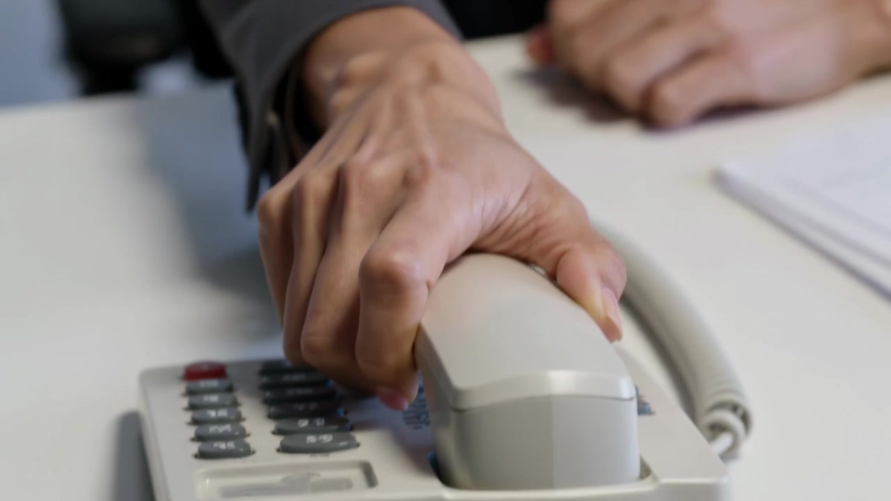 Receiving bad call, woman in gray blazer listening at office desk, gripping handset and ending call