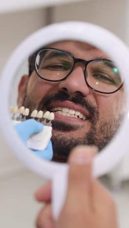 a smiling patient receives dental veneers as the dentist uses a precise shade guide to match tooth color, highlighting cosmetic care in a modern clinic.