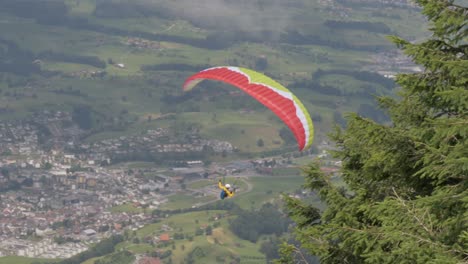 Slow-Motion-Paraglider-taking-off-from-hillside-turns-right-and-disappears-behind-pin-trees-on-Brienzer-Rothorn,-Switzerland