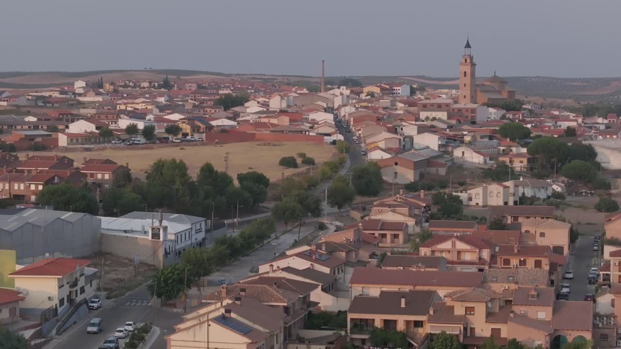 vuelo inverso y descenso con dron viendo parte de la ciudad de cebolla en toledo, tenemos como referencia la llamativa torre de su iglesia y apreciamos una de las principales calles