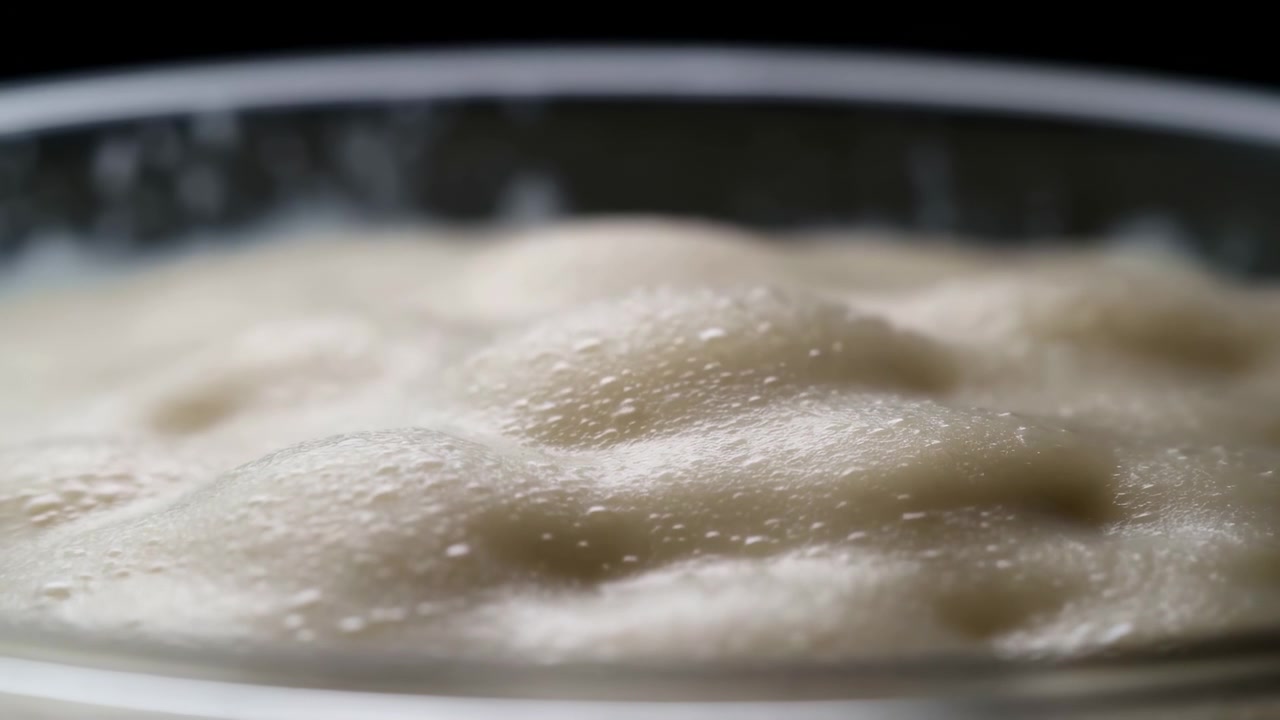 Close-up bubur hangat dalam mangkuk kaca pada pertengahan adegan, menunjukkan tekstur mendidih perlahan dan uap.