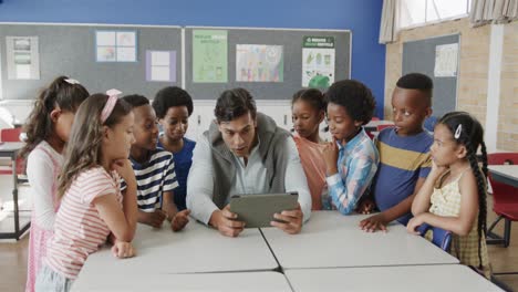 Happy-diverse-male-teacher-and-children-using-tablet-in-elementary-school-class,-slow-motion