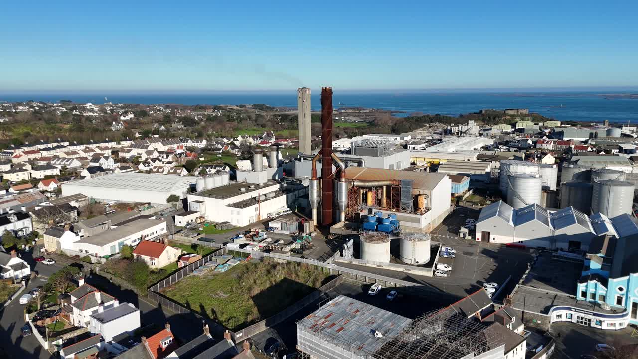 Dramatic drone reveal of Guernsey Power Station set in the middle of industrial area of St Sampsons with its chimneys in late afternoon sun and views across to Vale Castle and the sea beyond