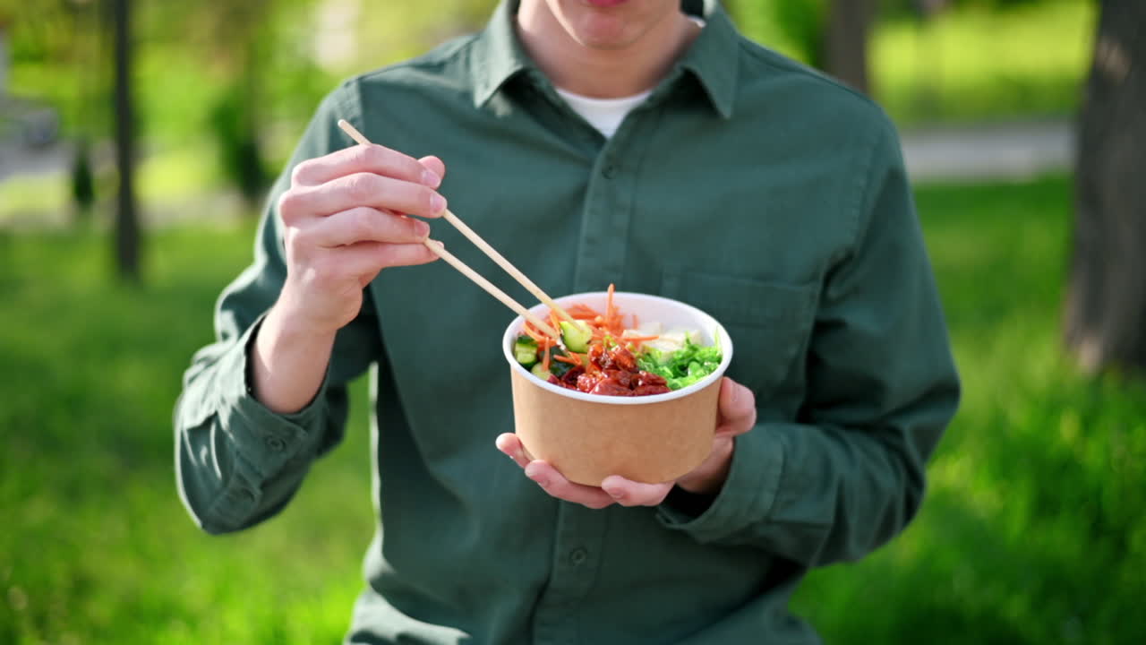 箸を使って、野菜、フルーツ、海藻サラダが入ったポキボウルを食べる男性のクローズアップ。スローモーション。