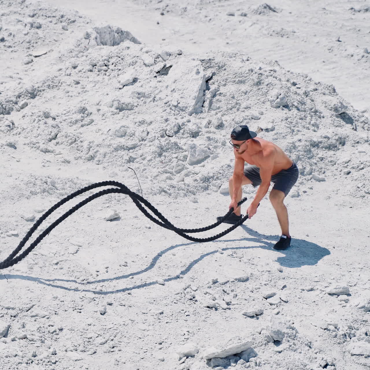 Happy sportsman finishing his workout with battle ropes outdoors. Topless athlete exercising with two ropes on the natural rocky background.