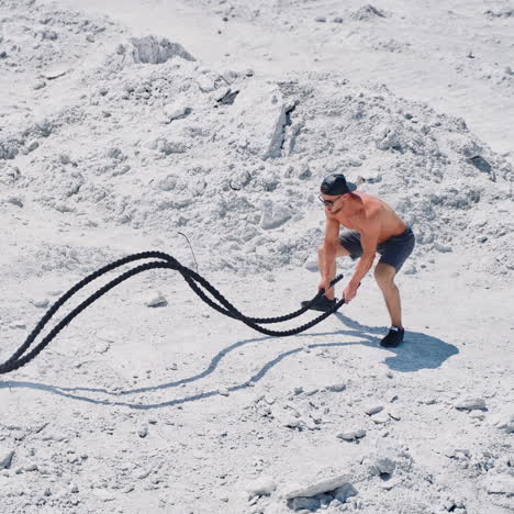 happy sportsman finishing his workout with battle ropes outdoors. topless athlete exercising with two ropes on the natural rocky background.