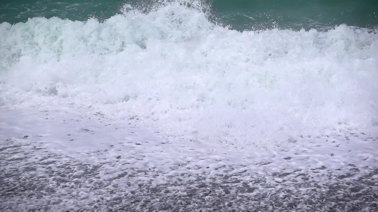 Powerful ocean waves crash in slow motion on a pebble beach during a storm, water splashing high