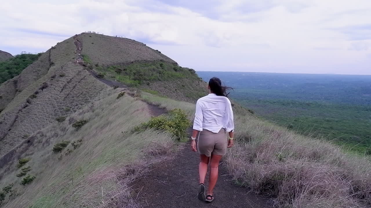 Woman walks on mountain summit ridge trail in high winds, slo mo