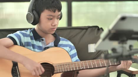 a boy learning to play the guitar, concentration on playing the music, little boy practicing some new sound on a guitar at home, boy having fun making music with guitar and singing along at home.