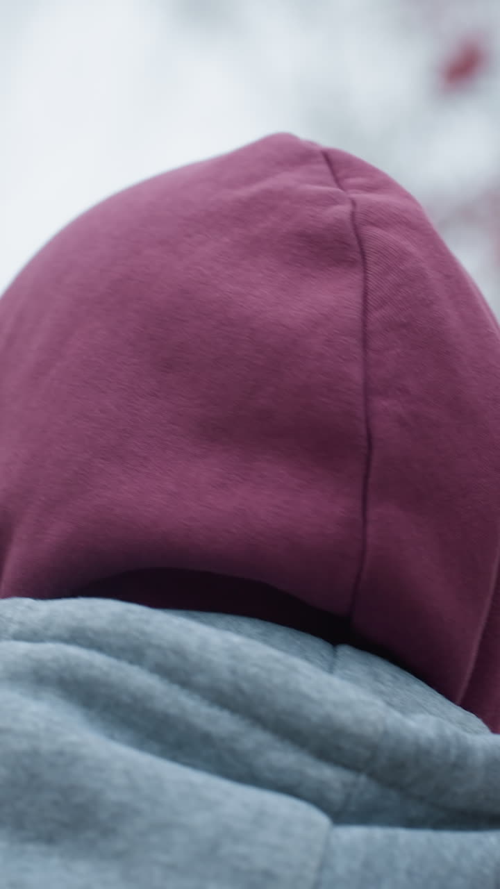 vista trasera de cerca de una persona que lleva una chaqueta con capucha marrón y gris caminando al aire libre, el fondo borroso presenta bayas rojas de enfoque suave y árboles desnudos