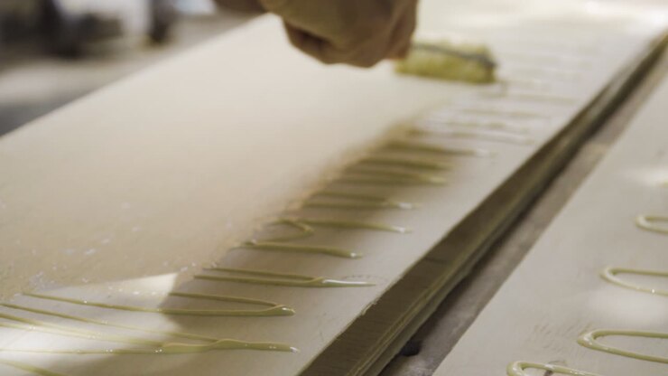 Close up, hands spreading glue on thin wooden plank with roller applicator in workshop