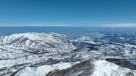 Aerial-pull-away-shot-of-top-of-Myoko-Mountain-Summit,-Japans-coast-line-and-ocean-sea-visible-in-background