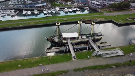 Drone-shot-of-a-historical-sailing-vessel-and-a-bustling-modern-port-in-Salem,-Massachusetts