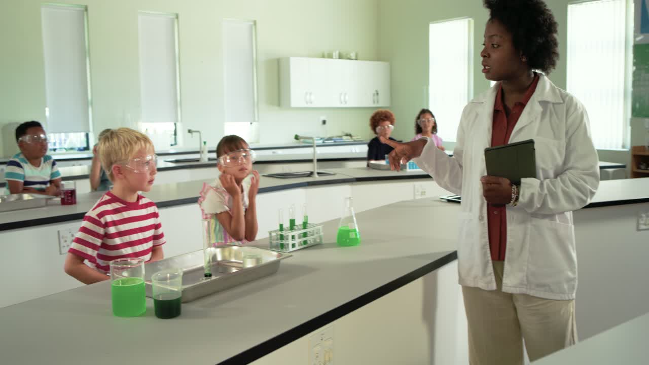 Un insegnante in camice da laboratorio indica e istruisce i bambini in laboratorio che indossano occhiali protettivi e osservano una miscela verde.