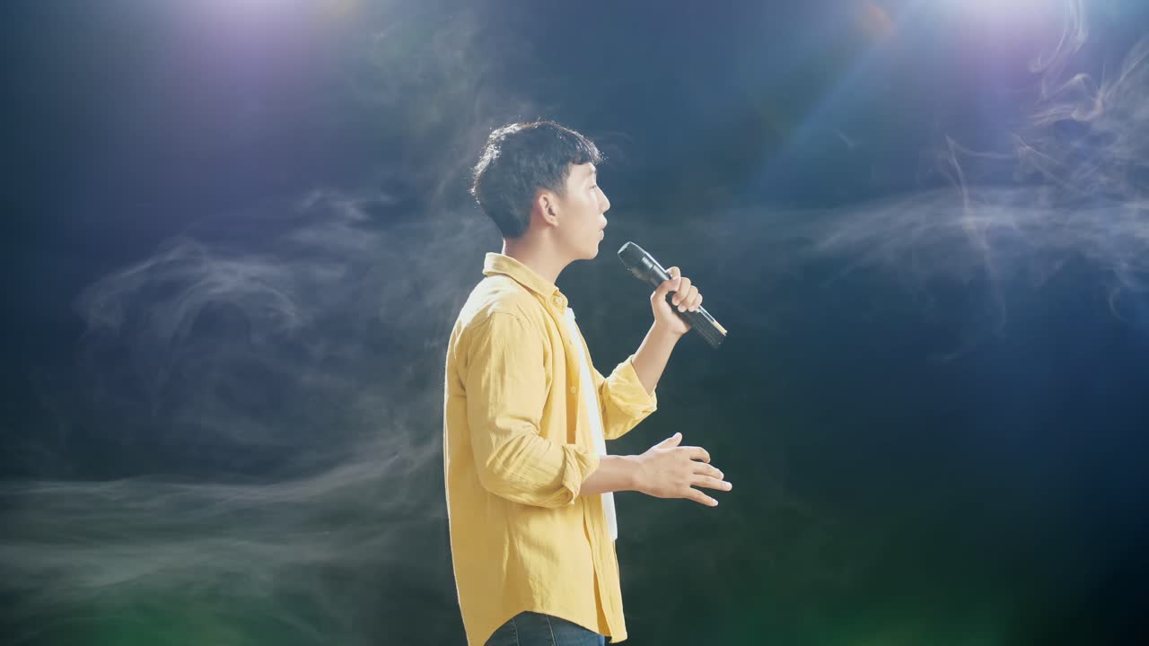 젊은 아시아 소년이 마이크를 들고  연기 검은 배경에서 노래하는 측면 시각