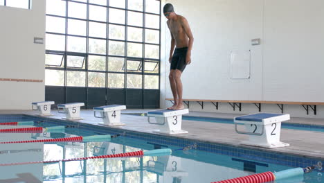 Young-biracial-male-athlete-swimmer-prepares-to-dive-at-an-indoor-pool