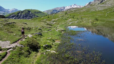 woman hikes wetlands trail along mountain lake in french alps - aerial follow