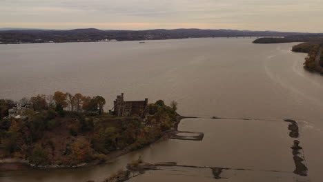 aerial drone camera flight towards bannerman's castle as it descends, trucks right - pans left, over the hudson river in beacon, ny on a cloudy, evening during sunset