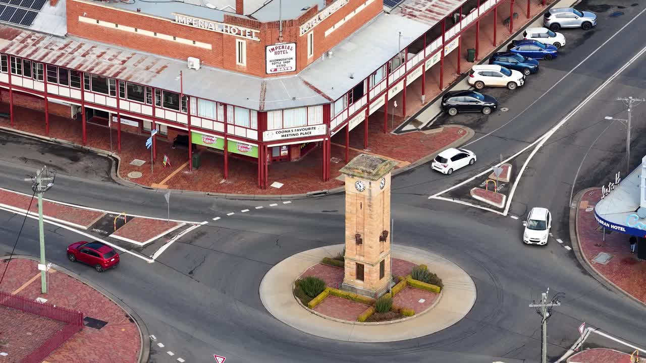 Aerial view of vehicles navigating a roundabout with a central clock tower in Coonabarabran, NSW, under natural daylight. Camera remains steady, capturing urban street activity