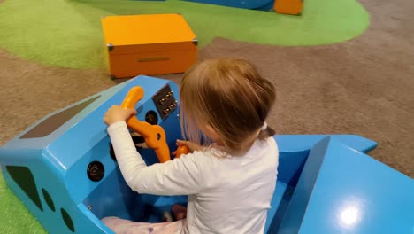 Cute-7-year-old-girl-playing-and-pretend-steering-wooden-toy-airplane-while-waiting-inside-airport-terminal-building---Handheld-moving-towards-and-around-child