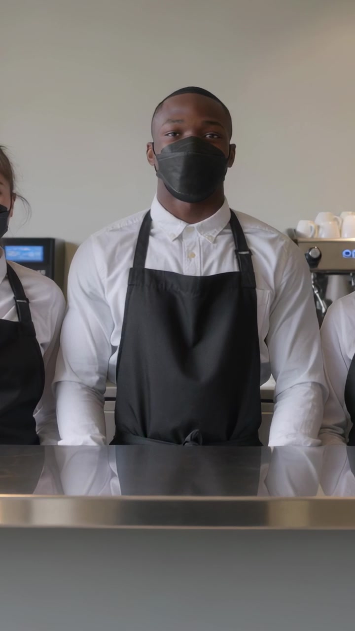 Video vertical: Grabando a un barista en el centro de pie detrás del mostrador con TPV, vistiendo uniforme y mascarilla.