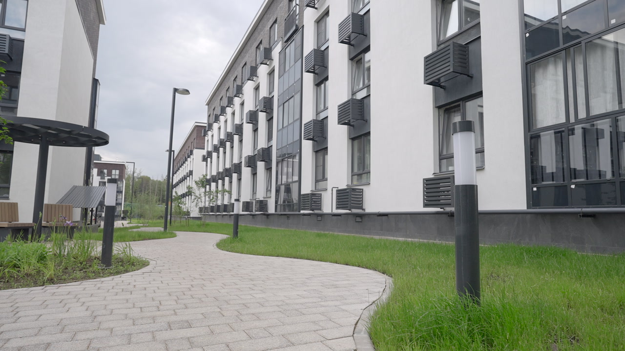 Curved Pathway Beside Modern Apartment Building, Empty Landscaped Courtyard With Lamppost And Green Grass