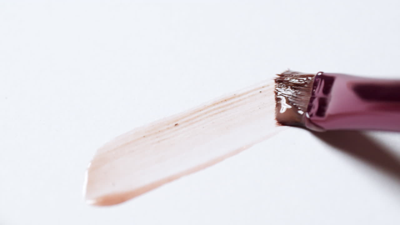 расчесывание слоя макияжа на чистой, белой палитре, чтобы проверить его текстуру и тон