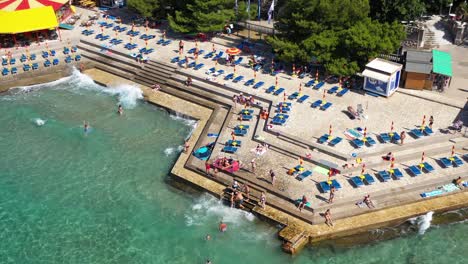 aerial view of people swims at adriatic sea with lounge chairs at novi beach in novi vinodolski, croatia