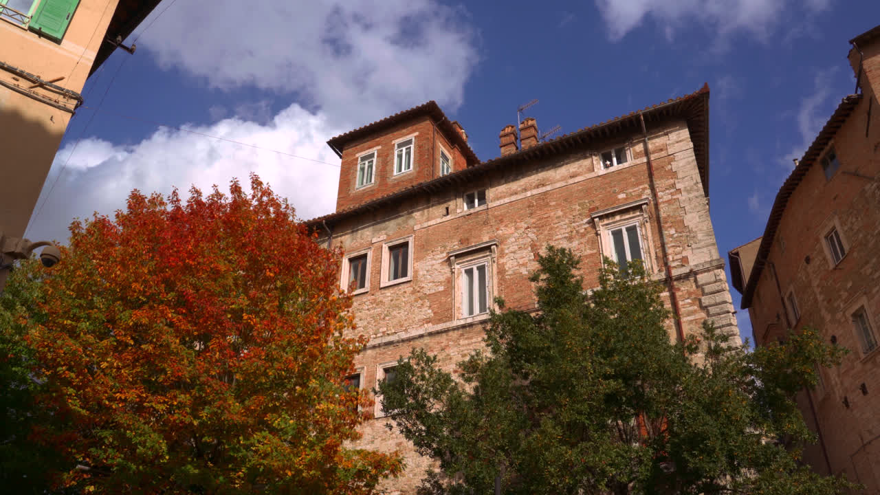 Historic brick church surrounded by autumn trees and blue sky in Perugia city center