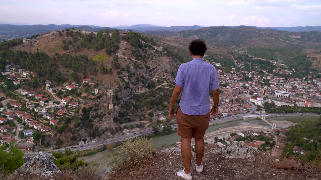 Male traveler standing high up on cliff, looking down at traditional village