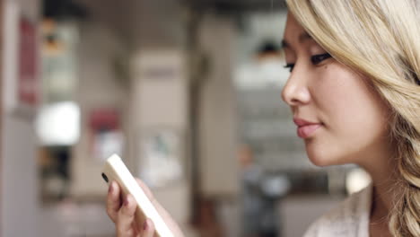 mujer asiática usando pantalla táctil de teléfono inteligente en una cafetería bebiendo café