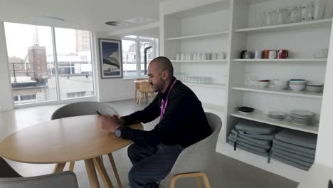 man in a modern kitchen using phone, natural light, casual attire, focused on screen, daytime