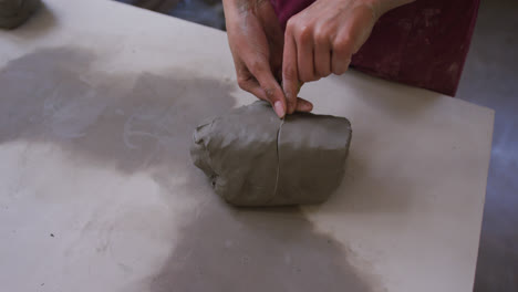 Close-up-view-of-female-potter-cutting-clay-with-thread-at-pottery-studio